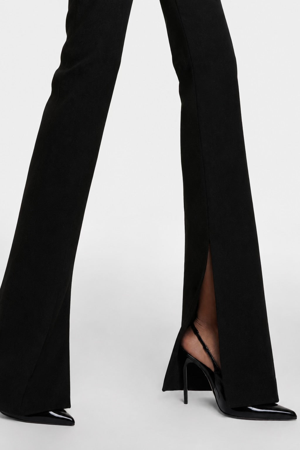 The Saint 54 Muse trousers in black with flared legs and inner seam slits, worn with black high-heeled slingbacks.