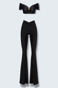 The Saint 54 black two-piece set featuring a cropped off-shoulder top with gold hardware and flared high-waisted pants.