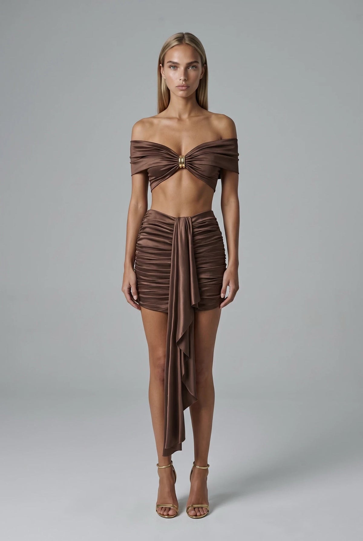 The Saint 54 brown two-piece set featuring a cropped draped top with gold hardware and a high-waisted ruched mini skirt.