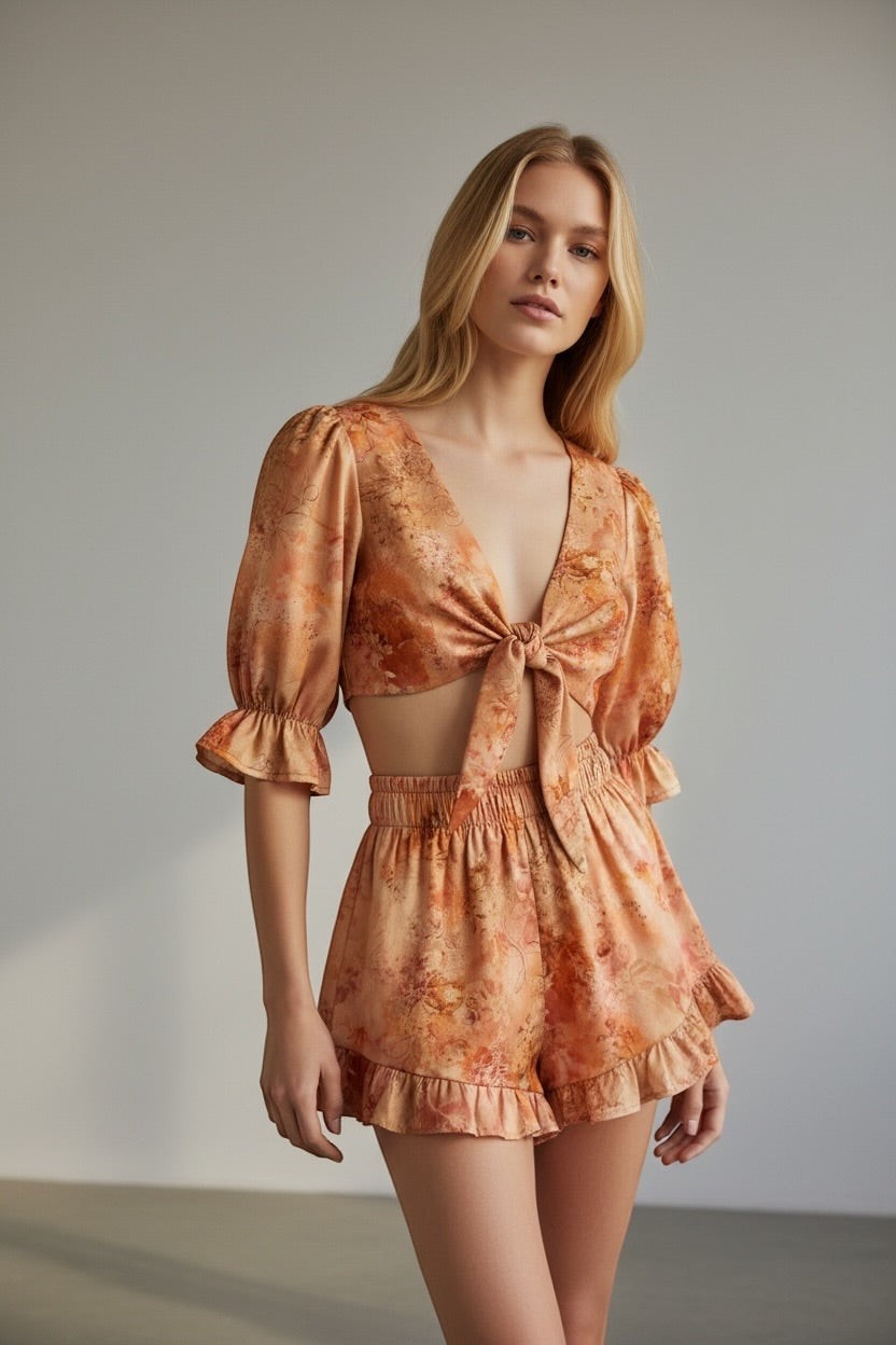 Model wearing The Saint 54 Sunset floral print two-piece set with tie-front puff sleeve top and ruffled mini shorts.