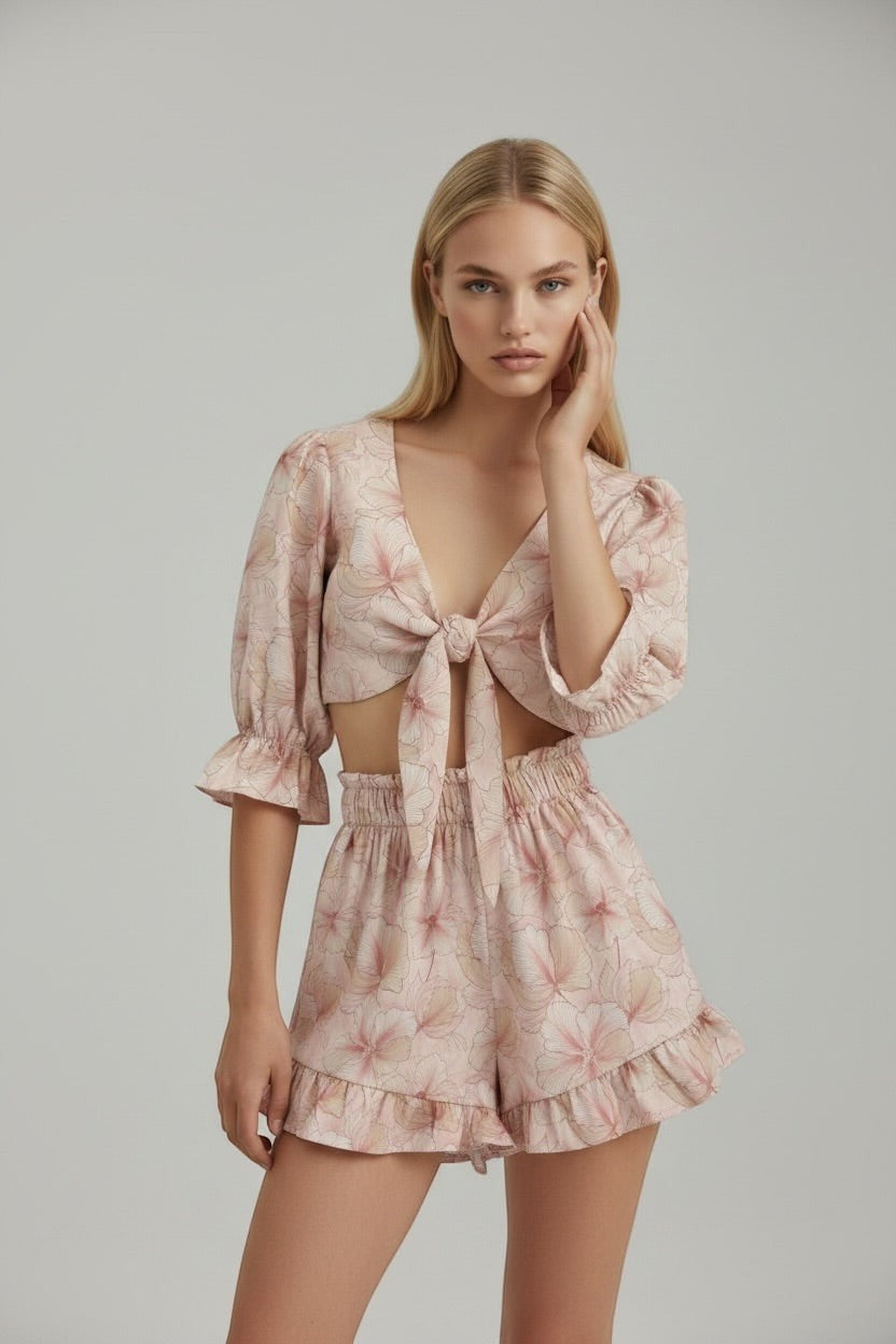 The Saint 54 pink floral two-piece set with tie-front puff sleeve top and high-waisted ruffled mini shorts on model.